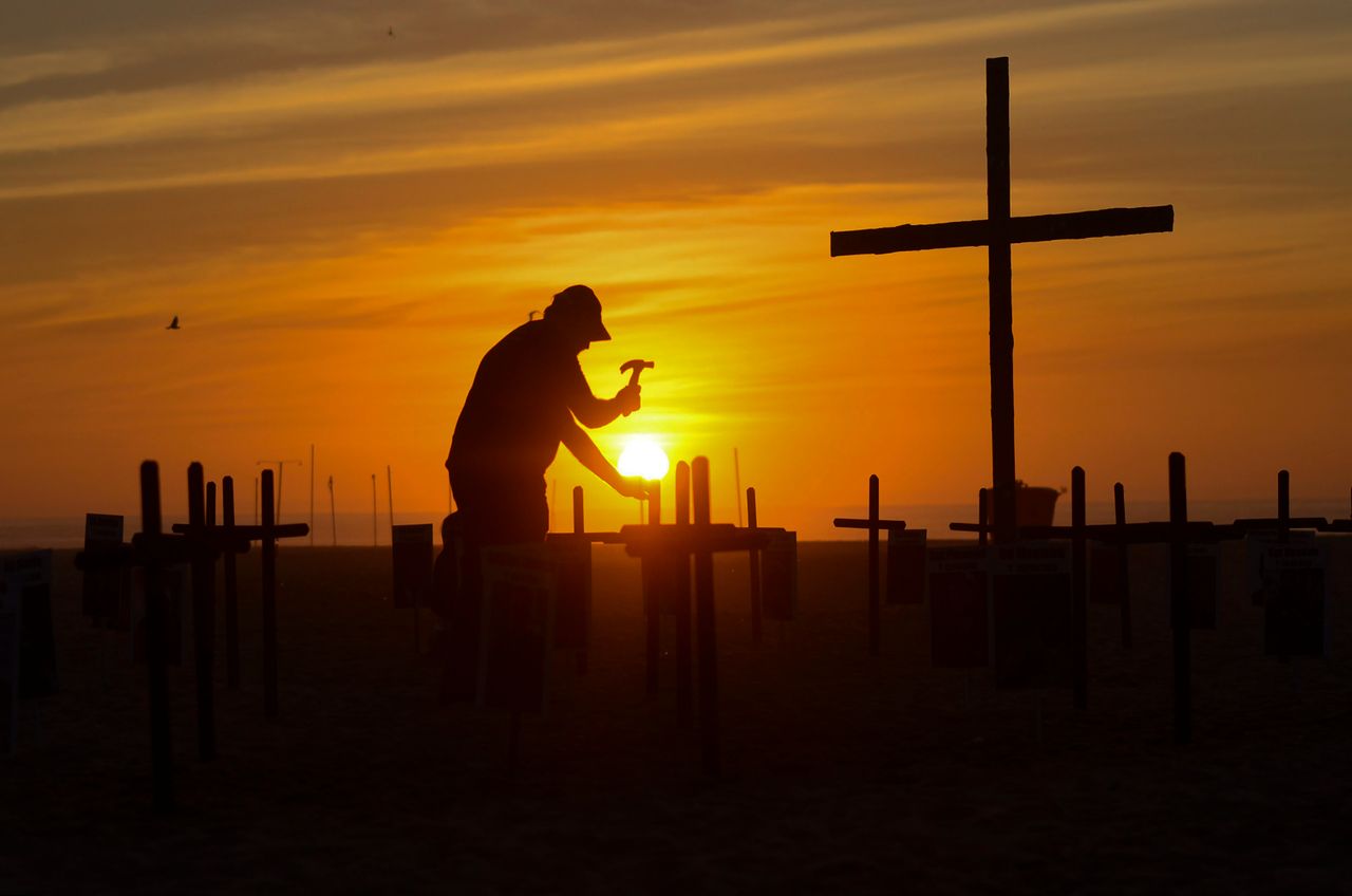 Dramatic silhouette of a man hammering at a grave as the sun sets in a Rio de Janeiro cemetery.